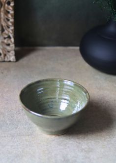 a green bowl sitting on top of a counter next to a vase