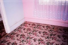 a room with pink walls and floral flooring in the corner, next to a window