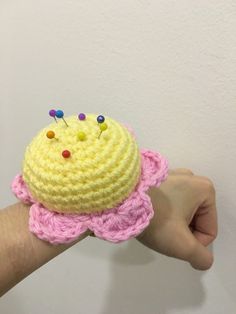 a hand is holding a crocheted yellow cupcake with pink flowers and pins