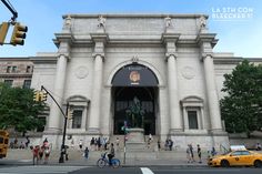 people are walking and riding bikes in front of an old building with a statue on it