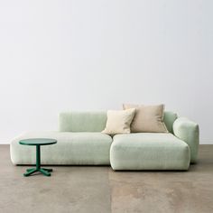 a green couch sitting on top of a cement floor next to a small round table