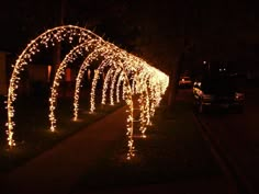 a row of lights on the side of a road at night with cars parked nearby