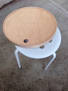 a wooden table sitting on top of a cement floor next to a white stool with holes in it