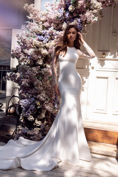 a woman in a white wedding dress standing next to a wall with flowers on it