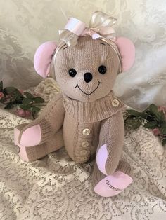 a brown teddy bear with a pink bow sitting on a white lace covered bed sheet