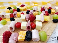 fruit and cheese kabobs are arranged on a cutting board with grapes, raspberries, melon, blackberries