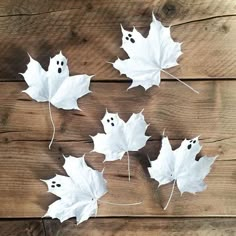 four white leaves with ghost faces on them are hanging from the side of a wooden wall