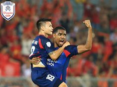 two soccer players are hugging each other in the middle of a game with an audience watching