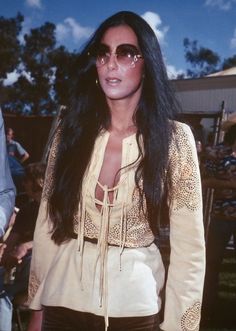 a woman with long black hair and sunglasses standing in front of a group of people