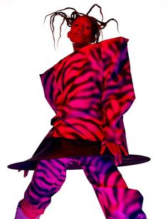 a woman with dreadlocks standing in front of a white background wearing a purple and pink zebra print coat