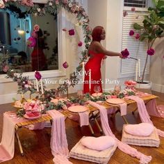 a woman in a red dress standing next to a table with pink and gold decorations