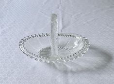 a clear glass dish on a white tablecloth with a silver handle and beaded edge