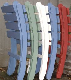 four different colored wooden chairs sitting next to each other on the ground in front of a building