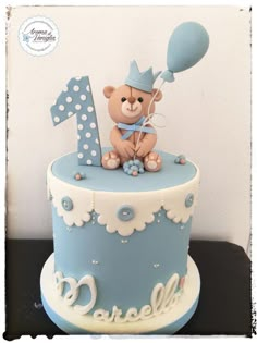 a blue and white birthday cake with a teddy bear on it's top tier