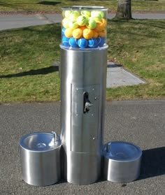 a water fountain with balls in it on the side of the road next to some grass and trees