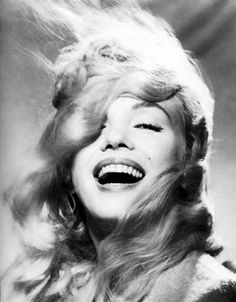 a black and white photo of a woman laughing with her hair blowing in the wind