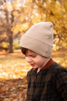 a young boy wearing a knitted hat in the fall with leaves on the ground