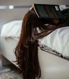 a woman laying on top of a bed with a book on it's head