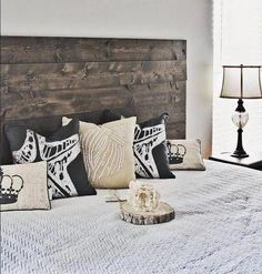 a bed with many pillows on it and a wooden headboard in the corner next to a lamp