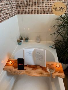 an open book on a wooden shelf in a bathtub with candles next to it