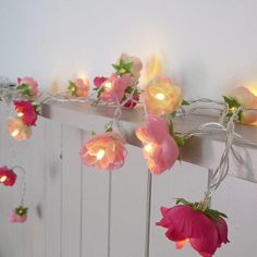 some pink flowers are hanging from a white wall with lights on it and there is no image here to provide a caption for