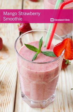 a strawberry smoothie in a glass with two strawberries on the table next to it