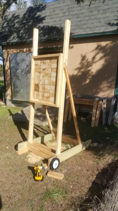 a wooden easel sitting in the grass next to a building with a window on it