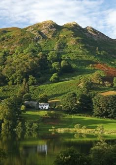 there is a mountain with trees and grass on the hillside next to it, as well as a body of water in the foreground