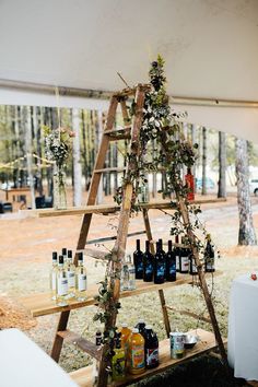 a wooden ladder with bottles and flowers on it in front of a picnic table under a tent