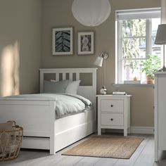 a white bed sitting next to a window in a bedroom under a light fixture on top of a wooden floor