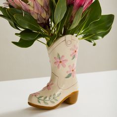 a vase with flowers in it sitting on top of a white table next to a pair of boots