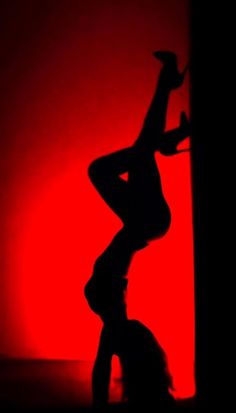 the silhouette of a woman dancing in front of a red background