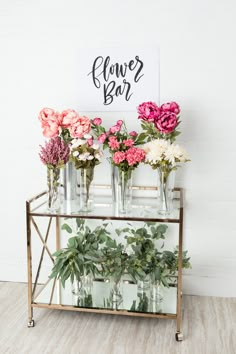 flowers are arranged in vases on a metal stand with a sign that says flower bar