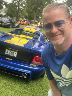 a man wearing sunglasses sitting in front of a blue sports car with yellow stripes on it