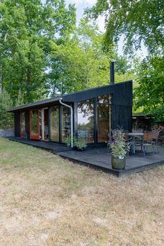 a small black cabin in the middle of a field with chairs and tables around it