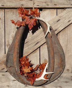 an antler and some leaves are hanging on a wooden wall in the shape of a horseshoe