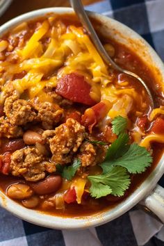 a white bowl filled with chili and meat soup on top of a checkered table cloth