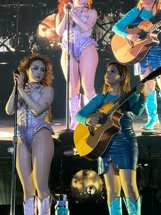 three women are performing on stage with guitars