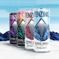 three cans of natural energy drink on a snowy surface with mountains and blue sky in the background