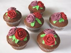 six cupcakes with chocolate frosting decorated with red and pink roses on them