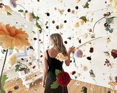 a woman standing in front of a wall with flowers on it and petals falling from the ceiling