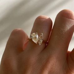 a person's hand holding a ring with two pear shaped diamonds on top of it