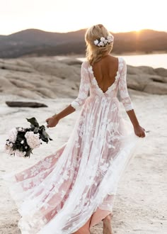 a woman in a white dress is walking on the beach with her back to the camera