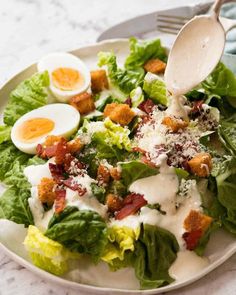 a salad with dressing being drizzled over it and topped with hard boiled eggs