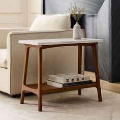 a table with some books on it in front of a couch and a vase filled with flowers