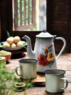 two cups and a teapot are sitting on a wooden table with food in the background