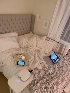 an unmade bed with two laptops and a candle on the end table next to it