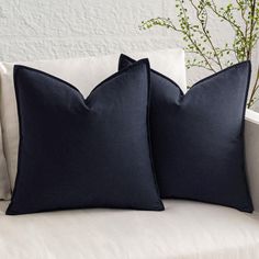 two black pillows sitting on top of a white couch next to a vase with flowers