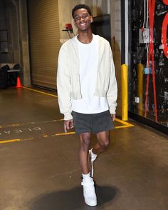 a young man is walking down the street in shorts and a white sweatshirt with his hand on his hip