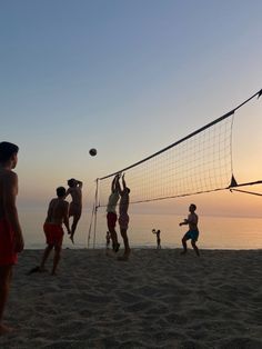 people playing volleyball on the beach at sunset